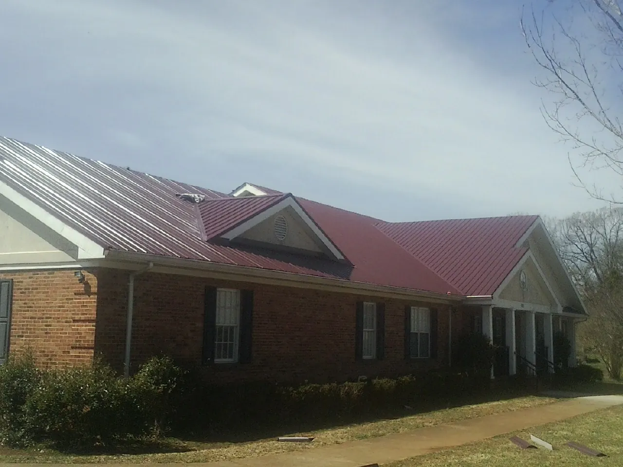 Red metal roof with gabled entries on a long brick building, from a Hail Damage Roof Repair job in Fort Covington