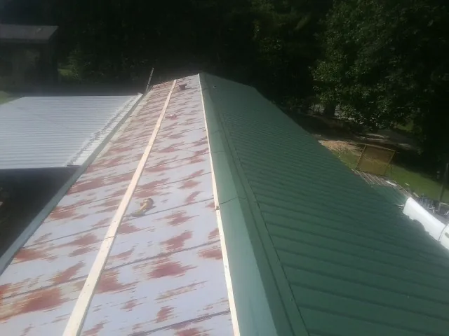 Old rusted panels beside newly installed green metal roofing — Wind Damage Roof Repair by Roofing Brothers in Fort Covington