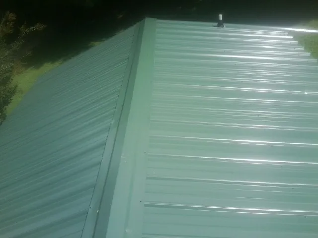 New green metal panels meeting at the ridge of a roof — Flat Roof Repair work by our crew in Fort Covington