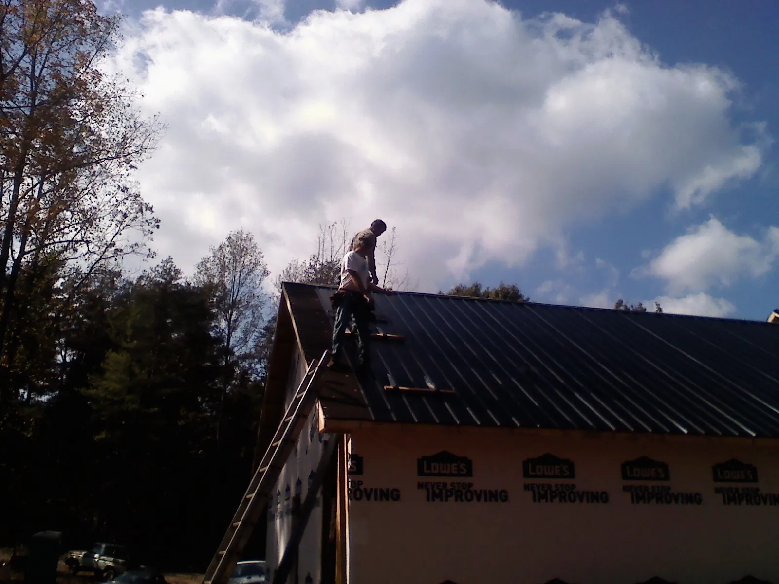 Roofer fastening dark metal panels high against a cloudy sky, from a Roof Inspection job in Fort Covington