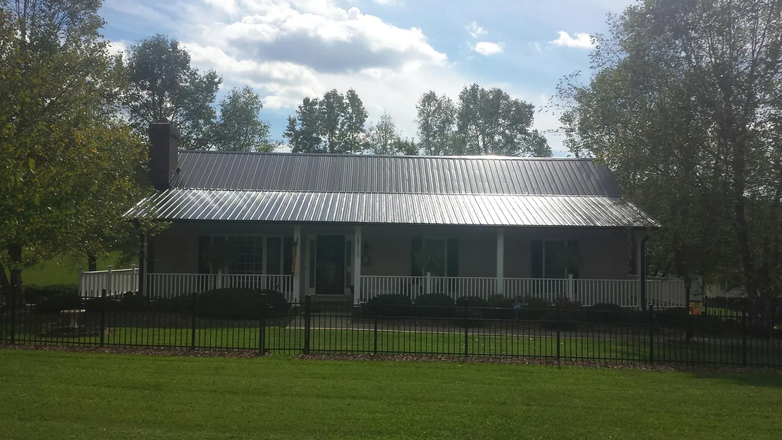 Gray metal roof on a brick ranch with a full width front porch — Gutter Guard Installation work by our crew in Fort Covington