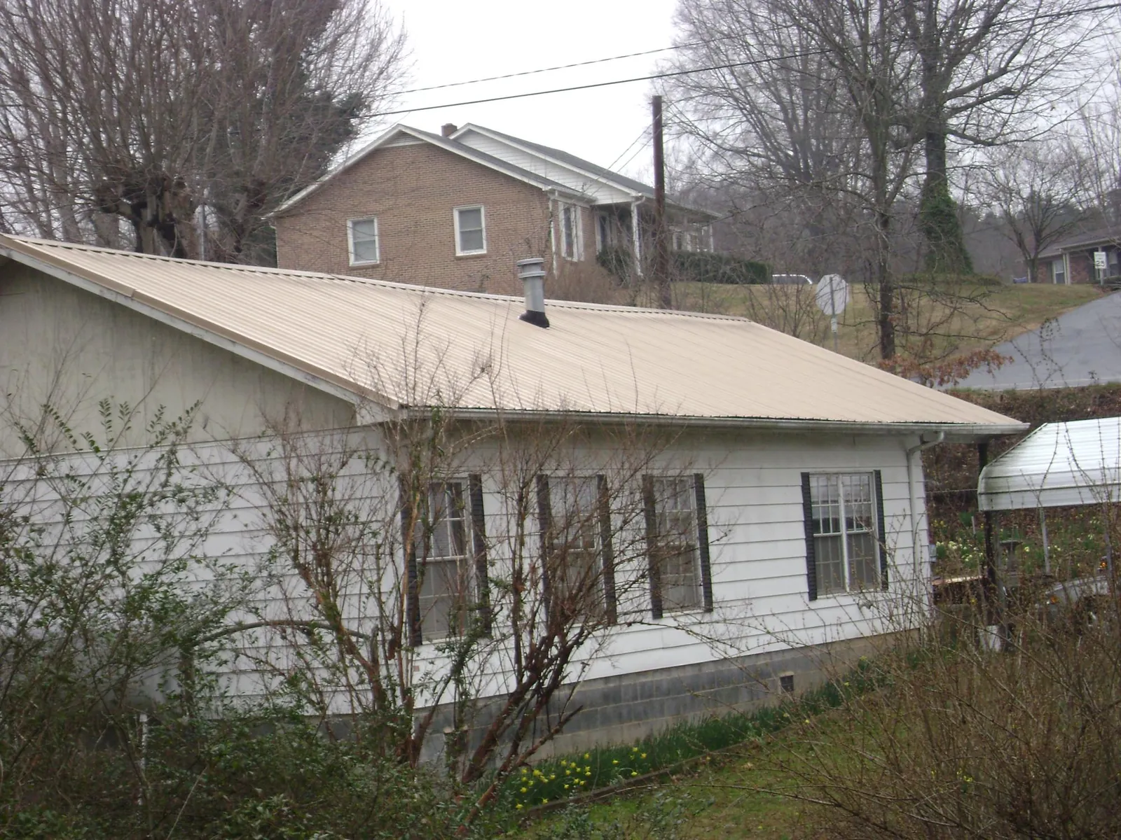 Tan metal roof on a white sided house set into a hillside — Commercial Roofing by Roofing Brothers in Fort Covington