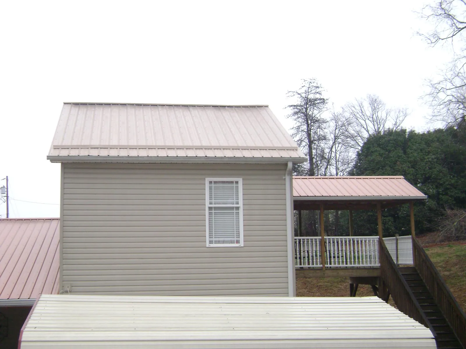 Tan metal roofs on a two story addition and attached porch, from a Roof Replacement job in Fort Covington